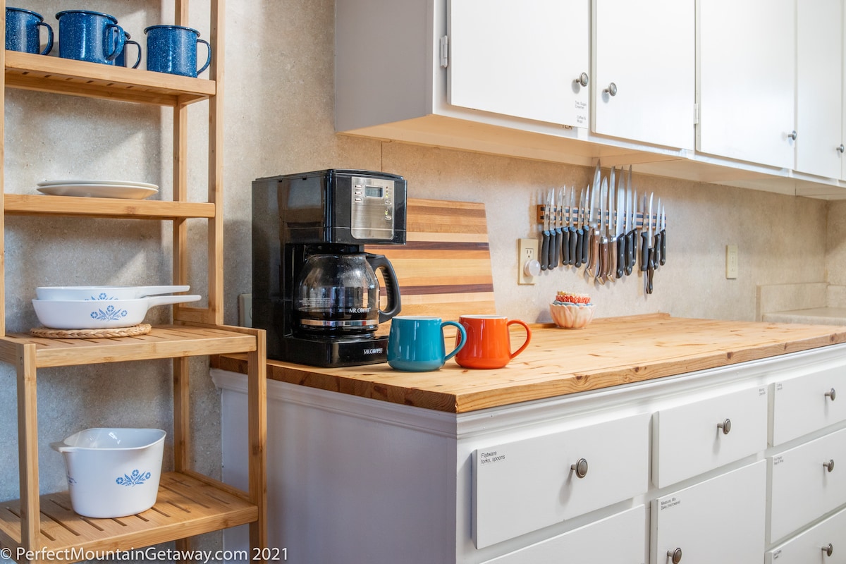 Kitchen with coffee maker, mugs, and utensils on the wall.